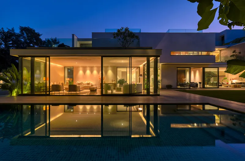 Glass pavilion reflected in the swimming pool at twilight with interior lighting glowing