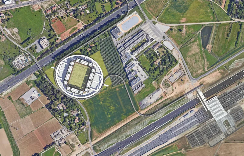 Aerial view of circular stadium with central pitch surrounded by green fields and agricultural plots