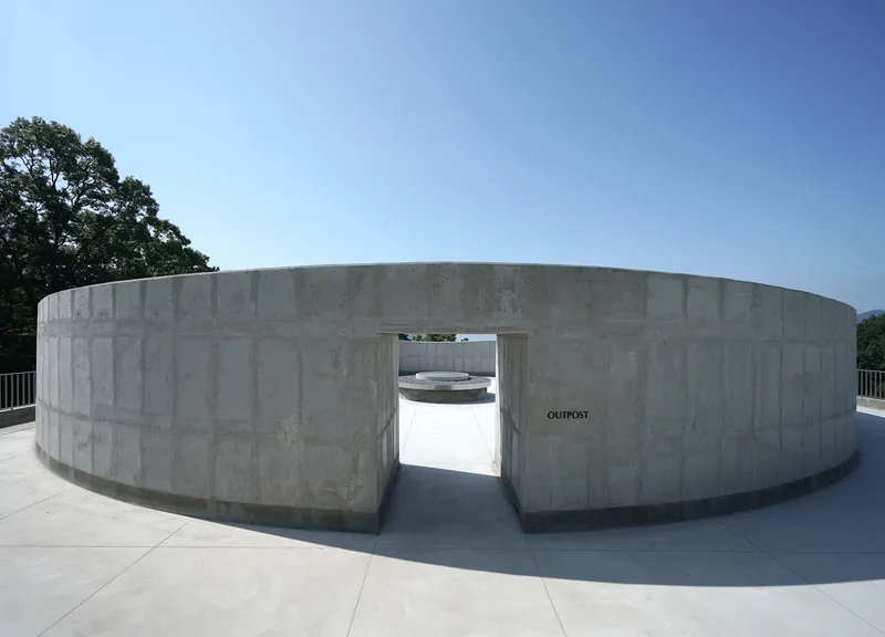 Circular concrete wall with central opening framing a view through to a courtyard under clear blue sky