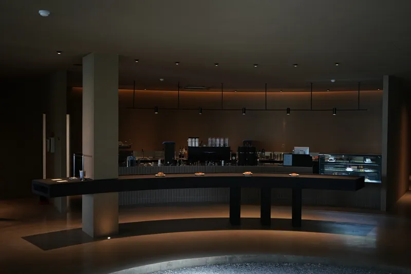 Dark interior cafe counter with warm linear lighting beneath suspended ceiling panels at dusk