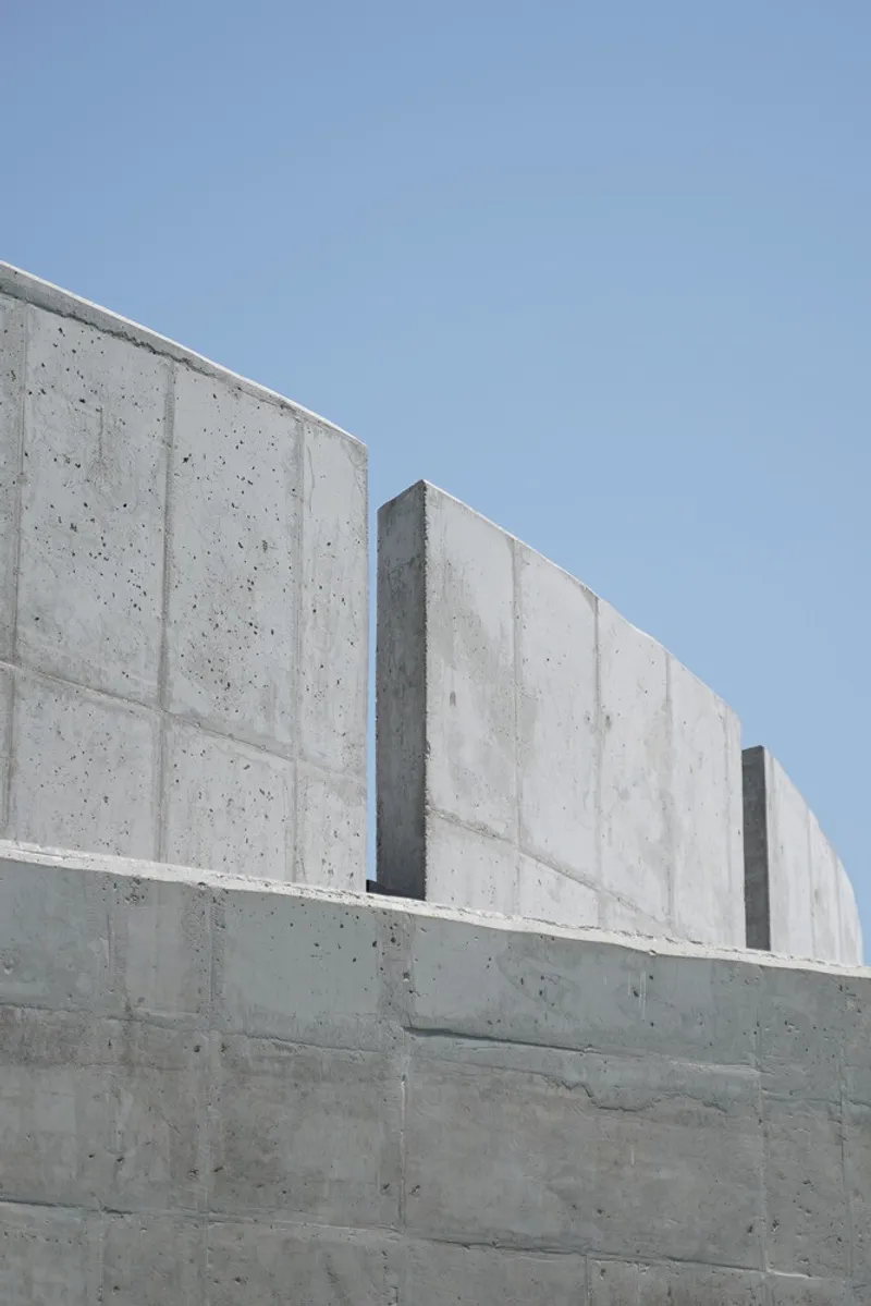 Upward view of stepped board-formed concrete walls with vertical panel joints against a clear blue sky