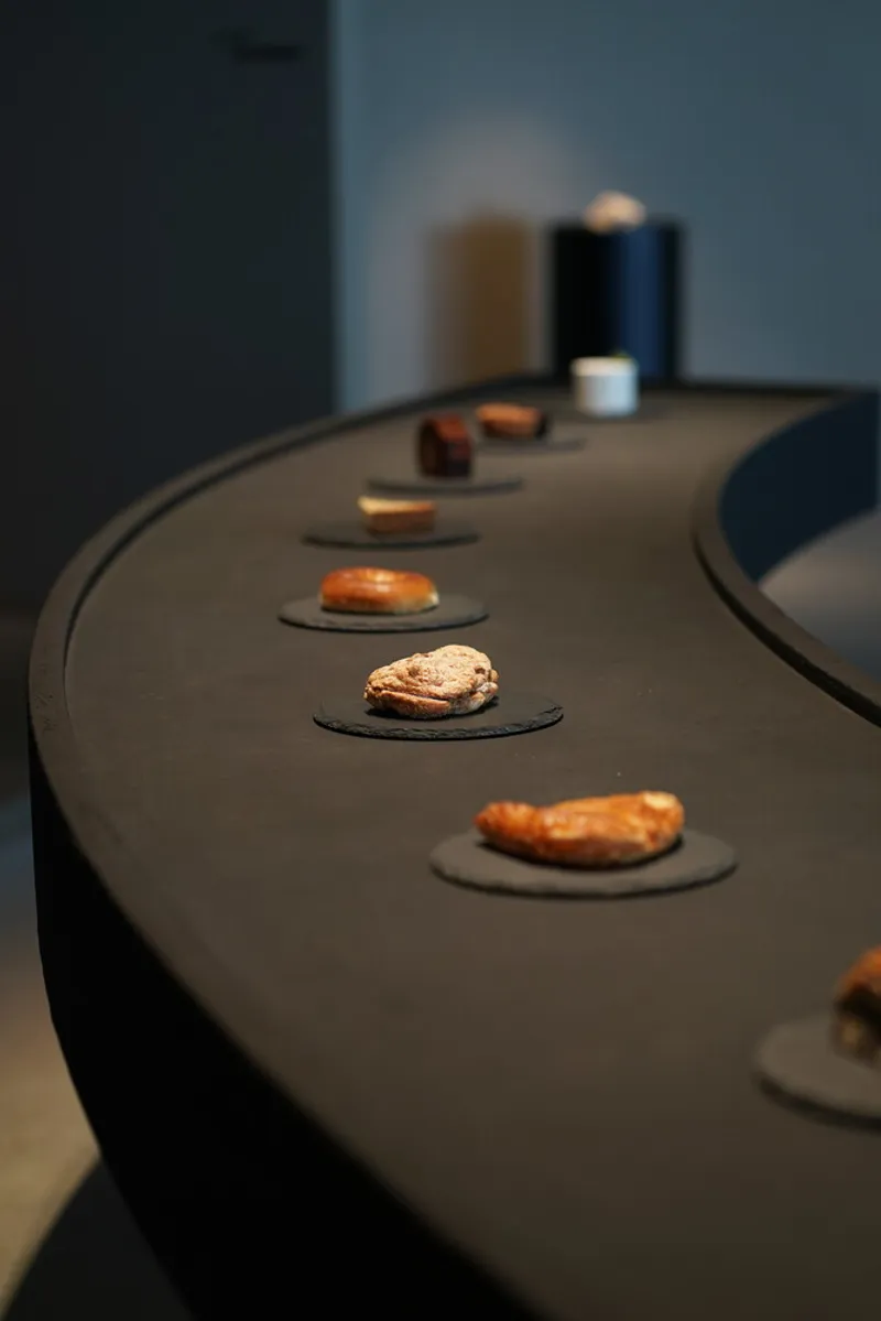 Close-up of curved black counter displaying baked goods on individual ceramic plates under soft light
