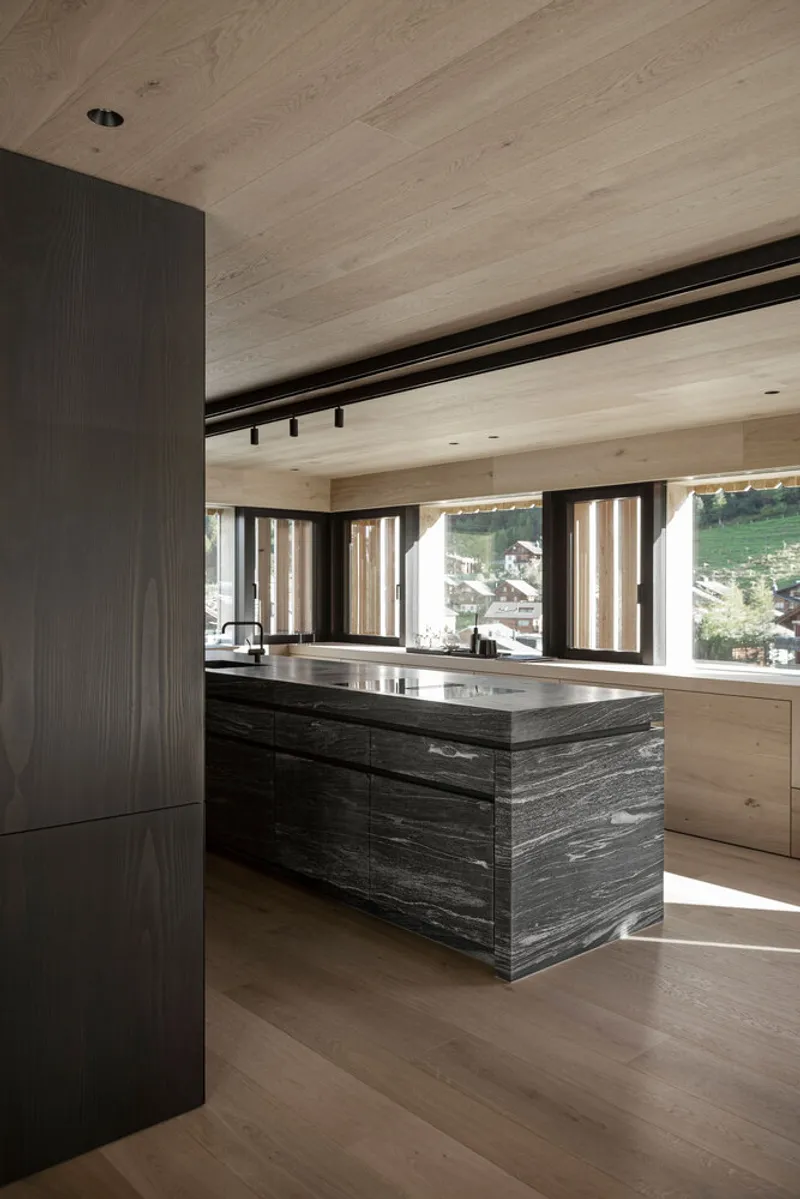 Kitchen island clad in dark striated timber beneath a pale wood plank ceiling with track lighting