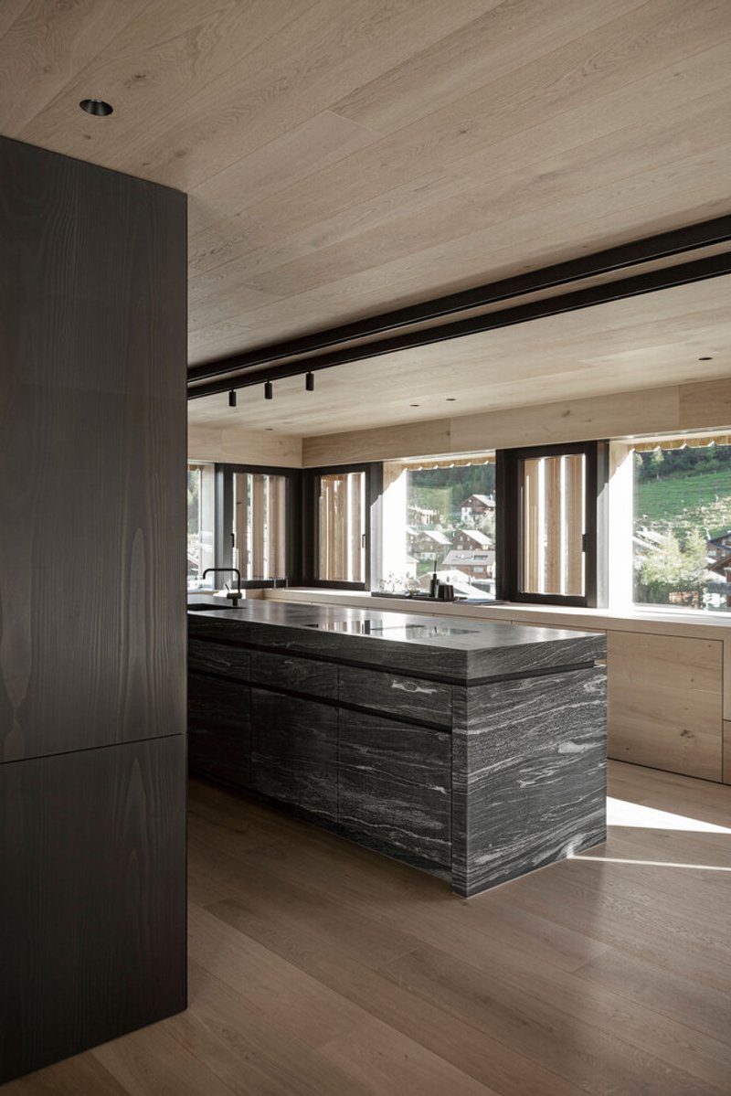 Kitchen island clad in dark striated timber beneath a pale wood plank ceiling with track lighting