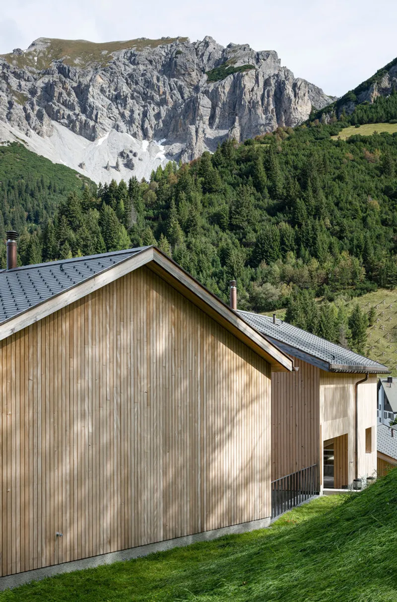 Timber gable end with vertical cladding set against forested slopes and exposed limestone cliffs