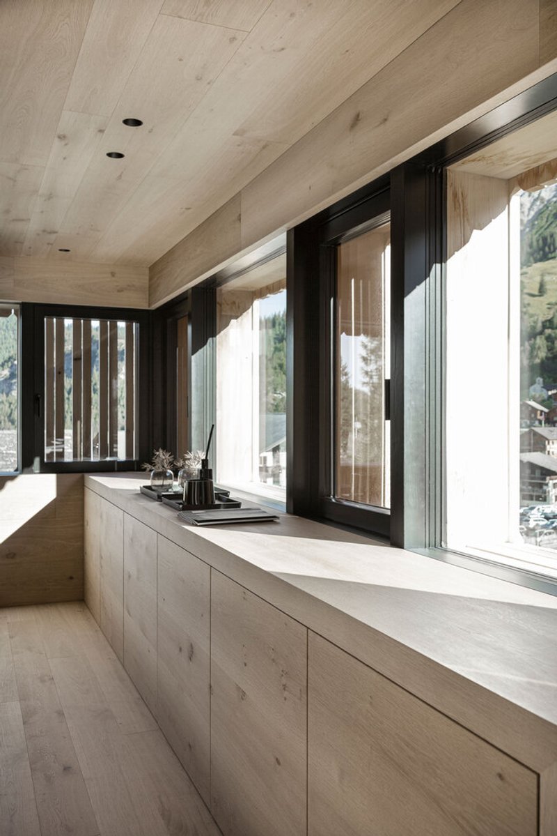 Pale timber countertop and cabinetry along a row of black-framed windows overlooking a hillside village