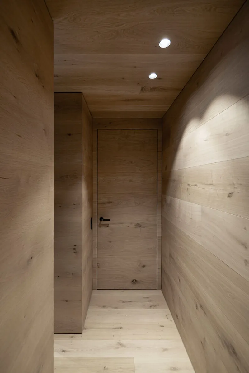Timber-clad hallway with flush door and recessed ceiling lights creating soft wall shadows at dusk