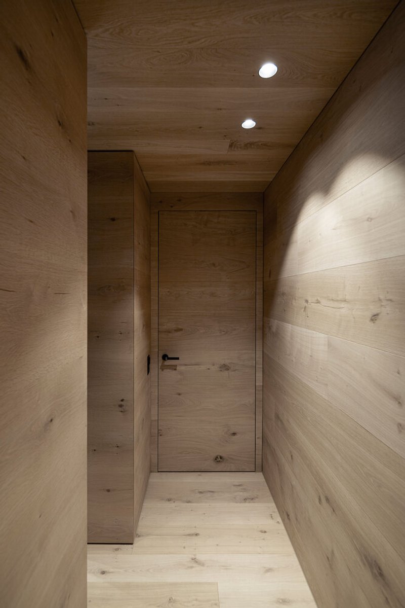 Timber-clad hallway with flush door and recessed ceiling lights creating soft wall shadows at dusk