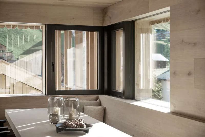 Built-in corner bench with vertical timber screens filtering light through black-framed windows onto the tabletop