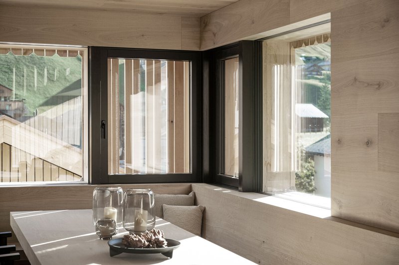 Built-in corner bench with vertical timber screens filtering light through black-framed windows onto the tabletop