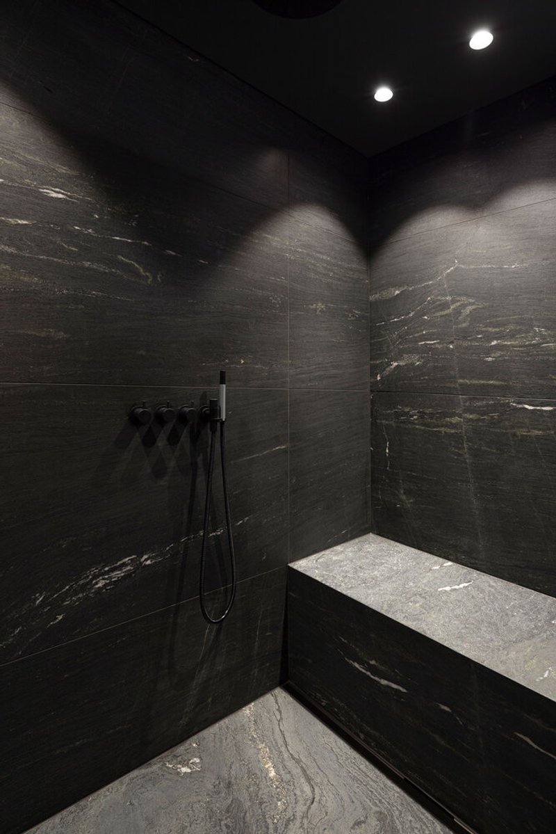 Dark stone-clad shower enclosure with recessed spotlights and integrated seating bench