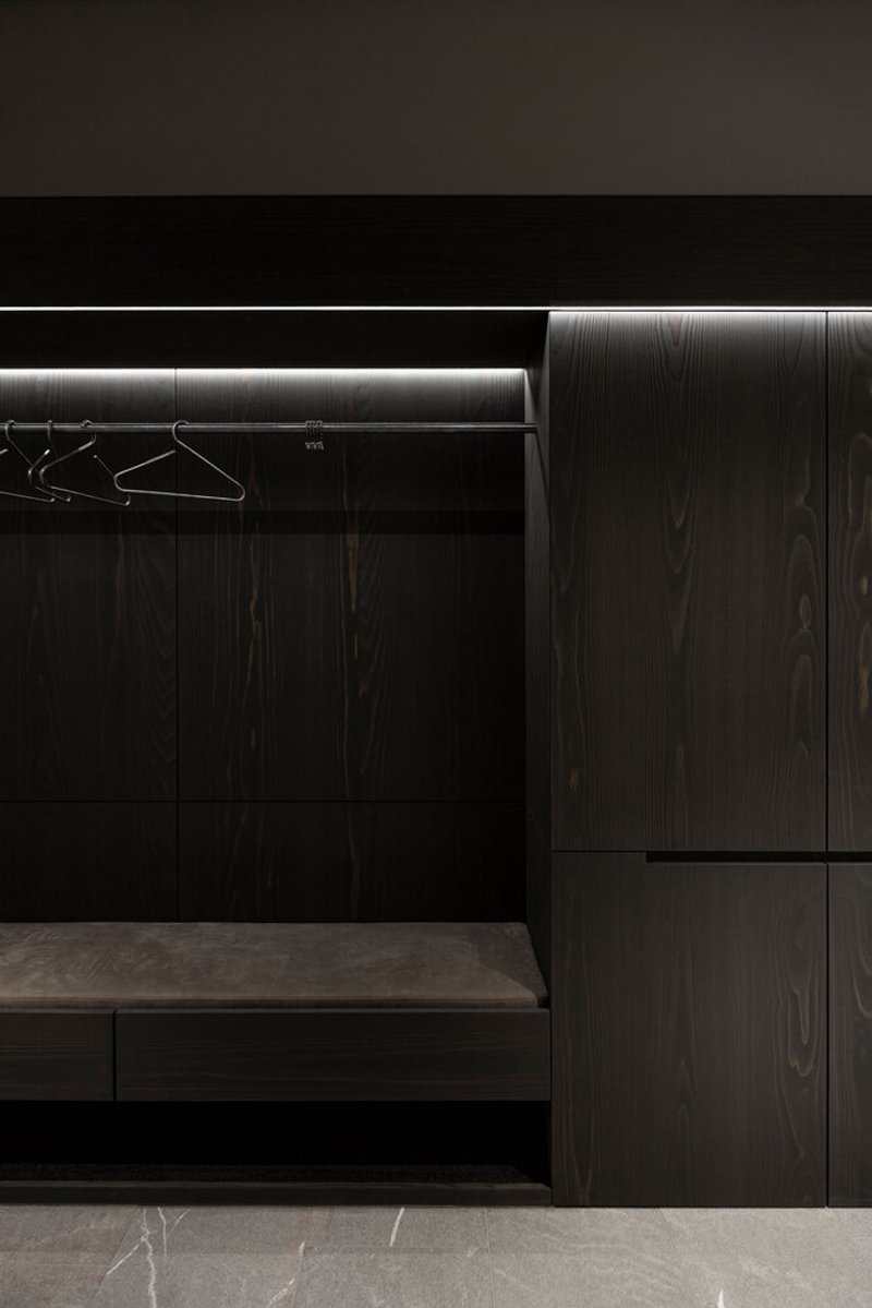 Dark timber veneer closet with illuminated hanging rail and wire hangers above a stone floor