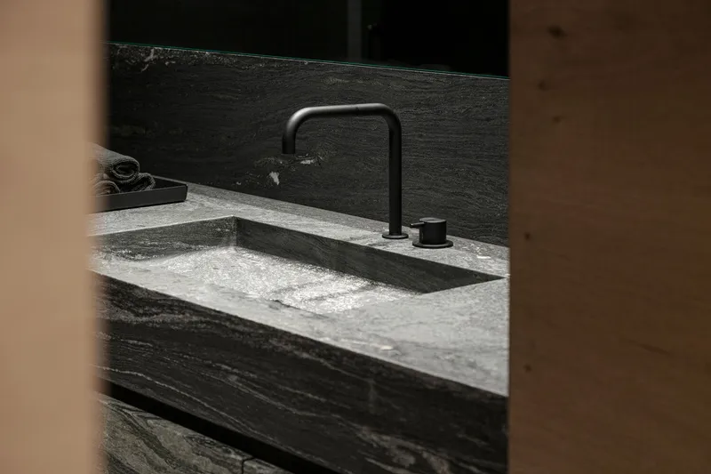 Close-up of matte black faucet against veined stone countertop framed by timber doorway