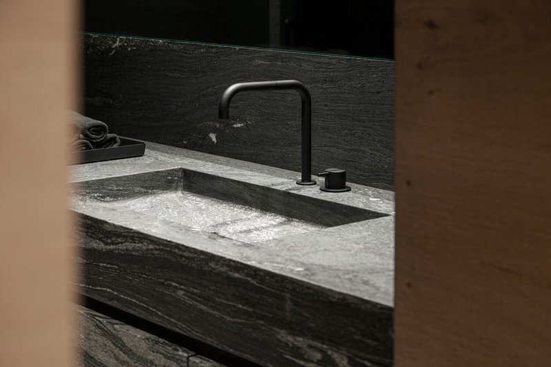 Close-up of matte black faucet against veined stone countertop framed by timber doorway