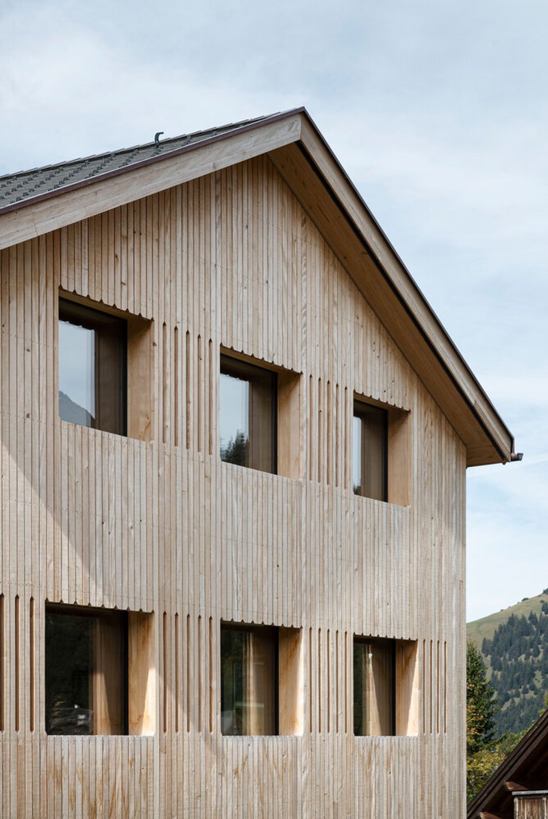 Vertical timber facade with recessed window openings under an overcast alpine sky