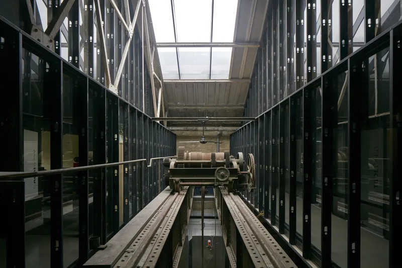 Looking up through the elevator shaft flanked by glass-walled corridors with exposed beams overhead