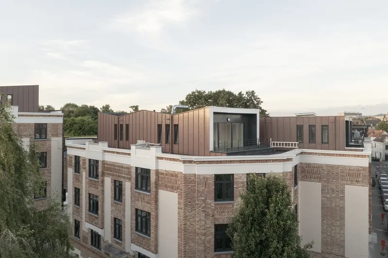 Rooftop view showing bronze metal cladding atop brick facades with trees in the background