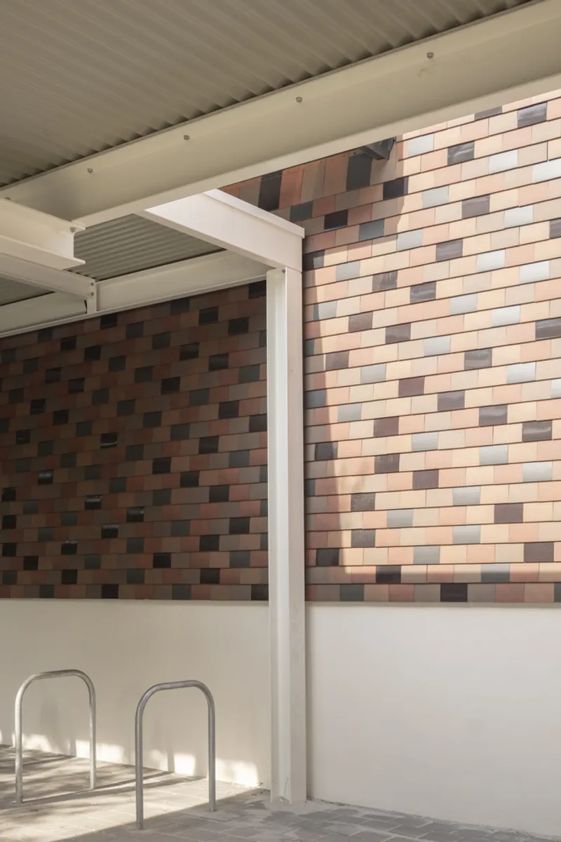 Covered parking area with white steel columns and multicolored brick tile wall