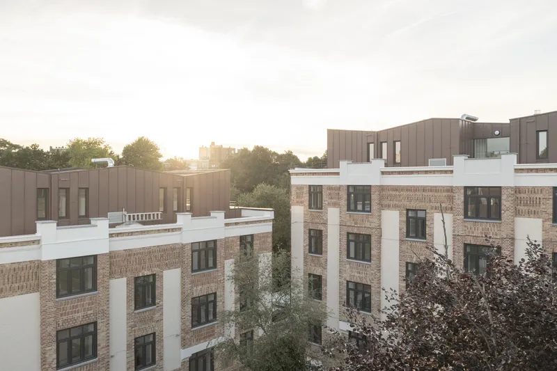 Courtyard view of paired residential blocks with buff brick facades and setback upper stories at golden hour