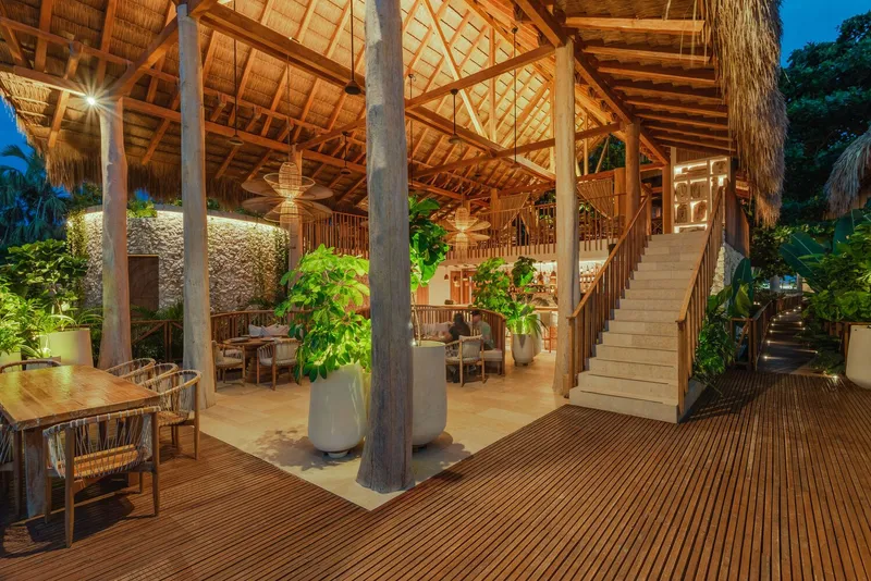 Open-air dining pavilion with thatched roof, concrete columns and timber decking at dusk