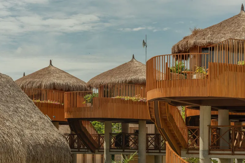 Cluster of circular thatched-roof volumes clad in vertical timber slats on concrete columns