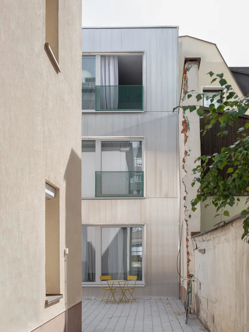 Narrow rear courtyard with corrugated metal facade, green balcony railings, and yellow bistro furniture