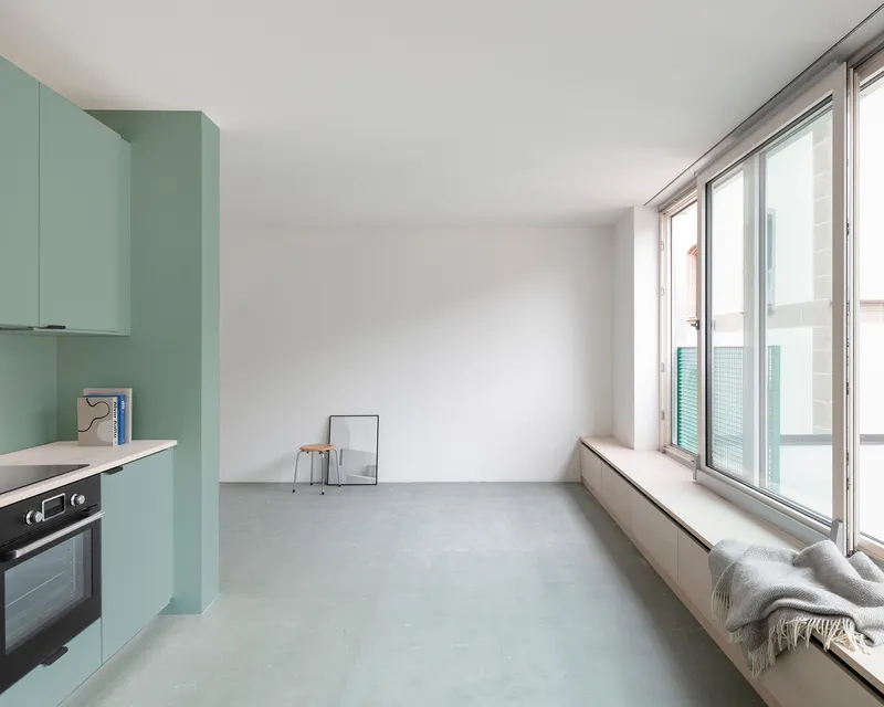 Open living space with pale green kitchen cabinetry, polished concrete floor, and window bench