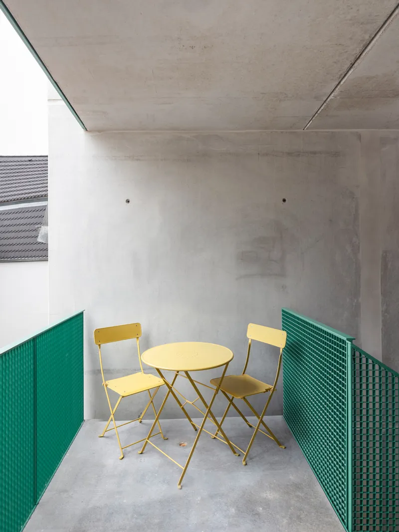 Balcony with exposed concrete ceiling, green perforated railings, and yellow folding table set