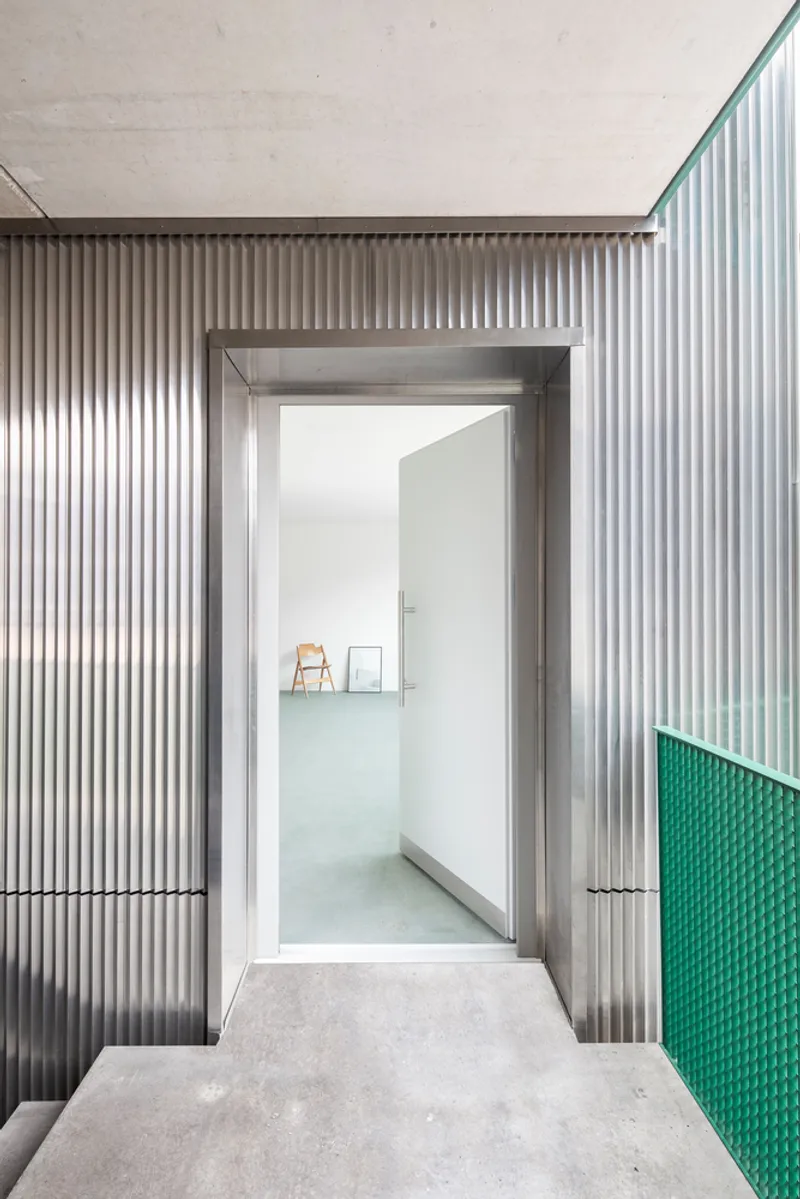 Recessed entrance with corrugated metal cladding and green perforated panel beside concrete floor threshold