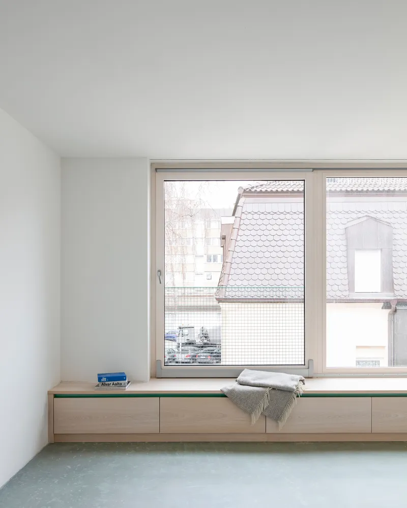 Window seat with timber storage drawers and folded blanket beneath a view of neighboring rooftops