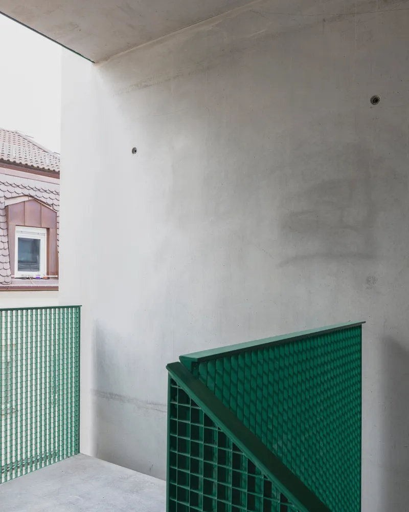 Corner detail of green perforated metal stair balustrade against concrete walls in natural light