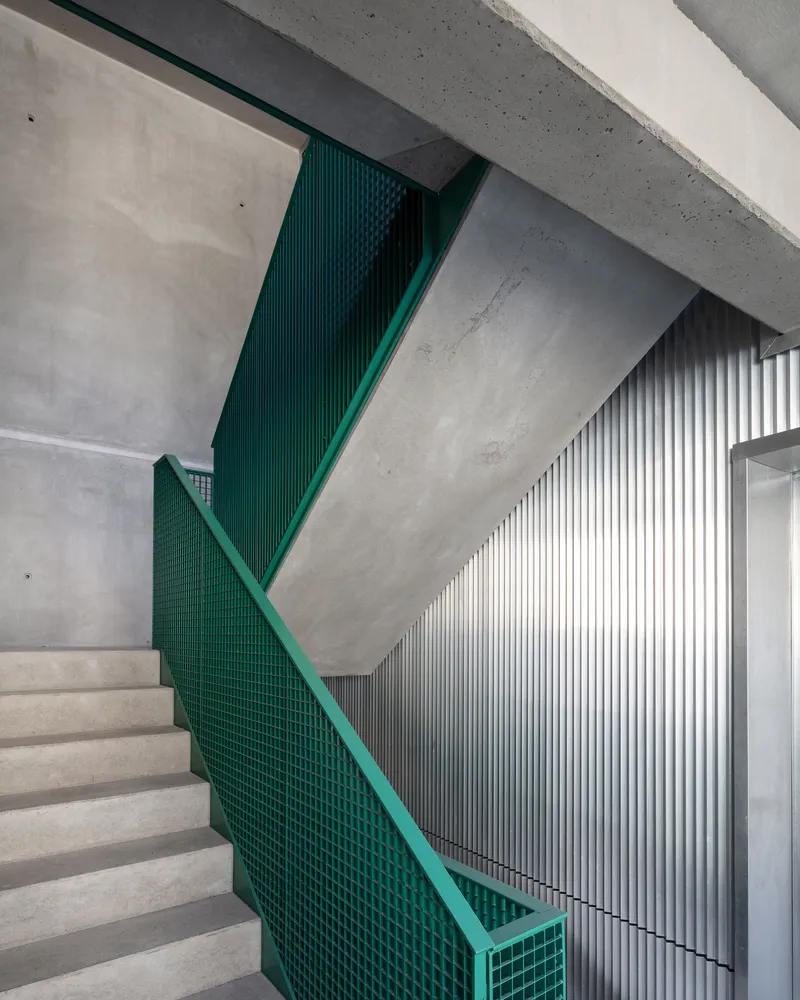 Staircase with green mesh balustrade and vertical metal slat wall beside concrete steps and soffit