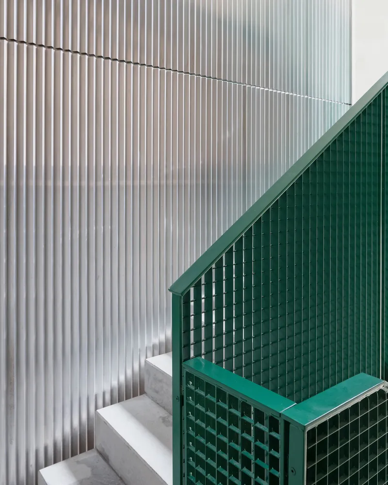 Stair railing intersection showing green gridded metal panels against fluted wall with diagonal cable detail