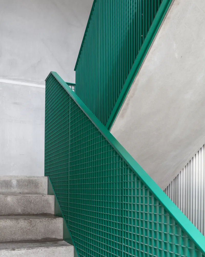 Green metal mesh stair balustrade with matching handrail adjacent to concrete steps and white walls