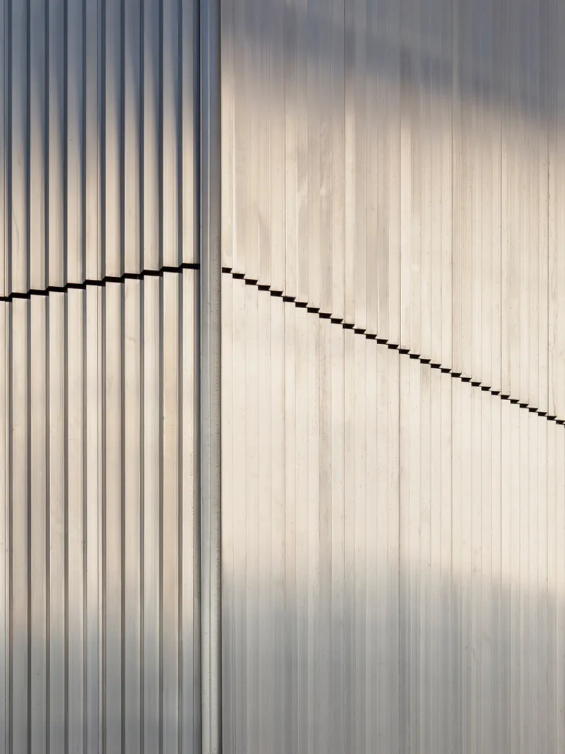 White vertical slat facade with diagonal shadow line cutting across the ribbed surface