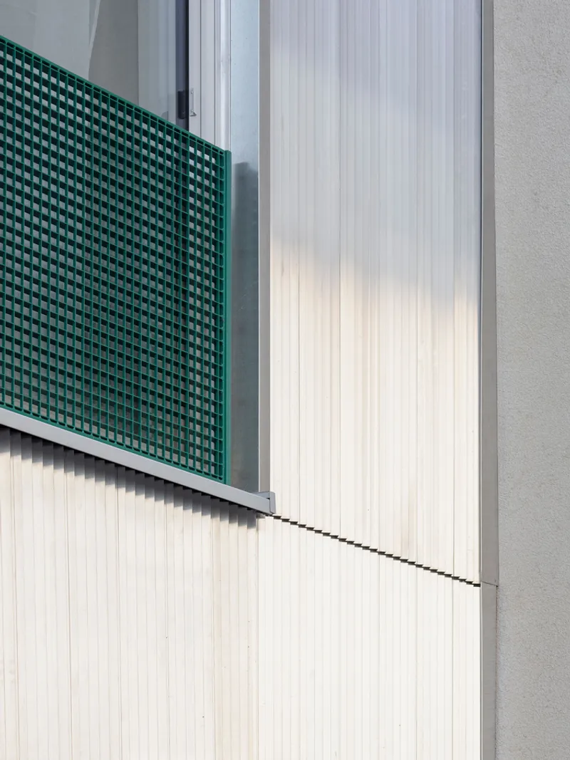Green perforated metal screen panel adjacent to white vertical ribbed cladding and concrete wall