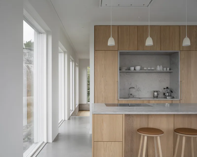 Kitchen island with oak cabinetry and concrete countertop beneath three white pendant lights