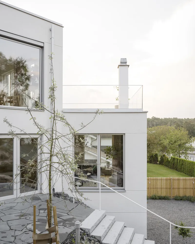 White rendered volumes with glass doors and a young tree in a planter on flagstone terrace
