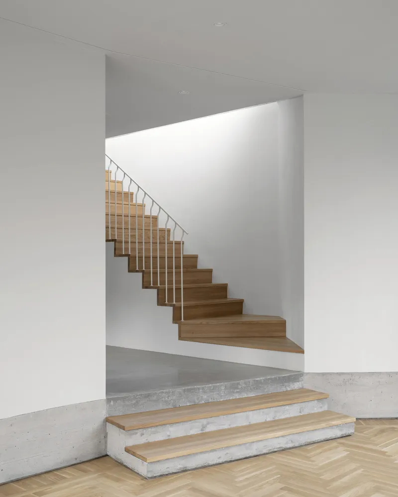 Timber staircase with vertical metal balustrades ascending through a white plastered volume with skylight above