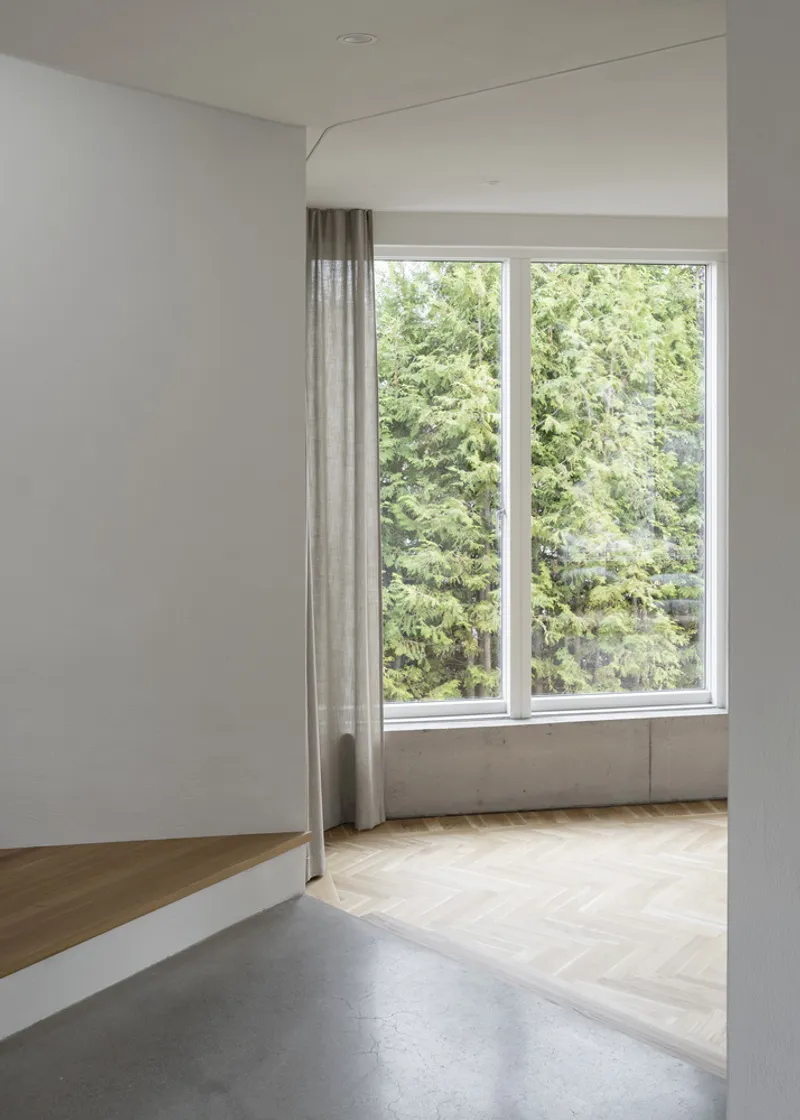 Herringbone oak flooring and concrete threshold leading to a window overlooking green trees in summer