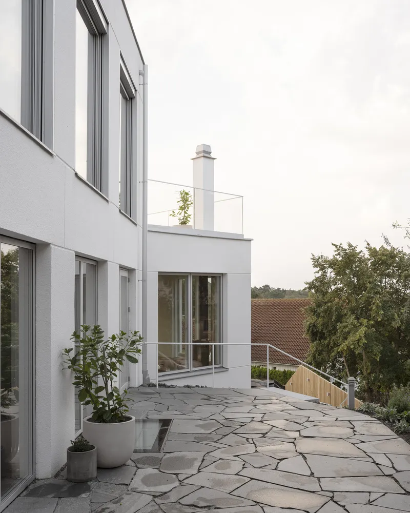 Rooftop terrace with irregular flagstone paving and potted plants beside white rendered facade and glass railings