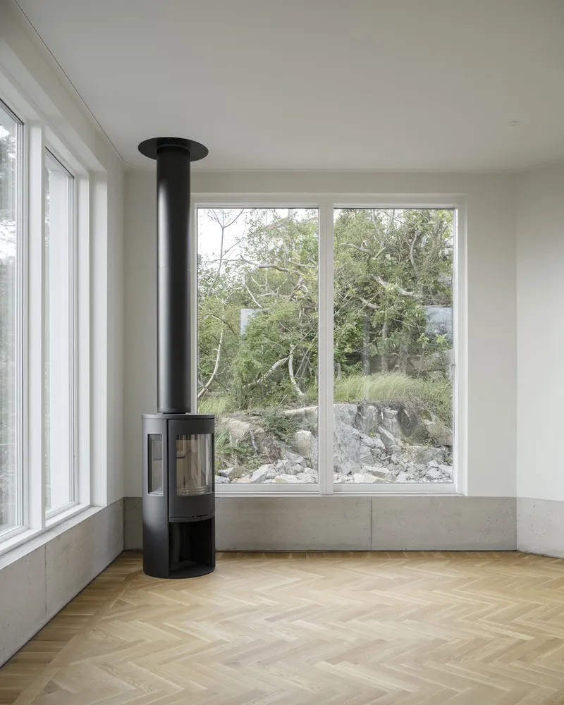 Cylindrical black stove in a corner room with herringbone oak flooring and views of rocky landscape