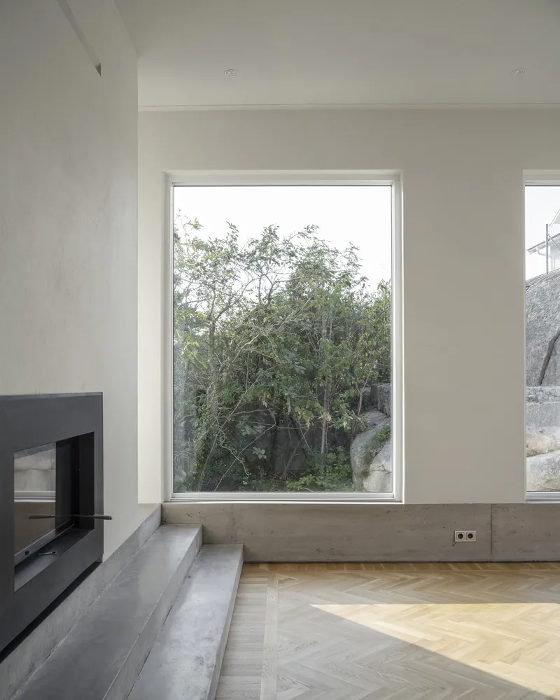 Floor-to-ceiling window framing trees and rocks beyond a concrete plinth and herringbone floor