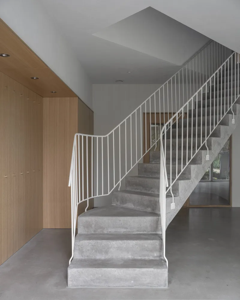 Curved concrete staircase with vertical white metal railing beside timber storage wall