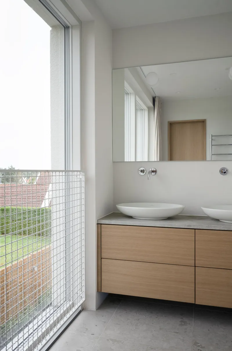 Bathroom vanity with twin vessel sinks and mesh-screened window overlooking residential rooftops