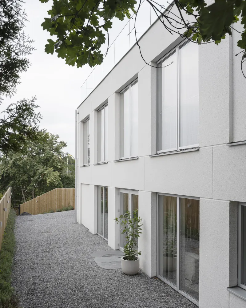 White rendered facade with tall windows and gravel courtyard framed by overhanging tree branches