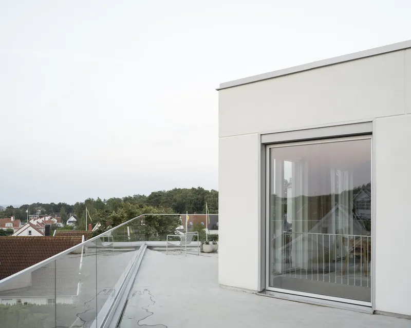 Rooftop terrace with glass balustrade and sliding door overlooking residential rooftops under an overcast sky