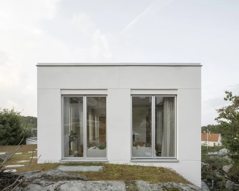 Flat-roofed white volume with paired glazed doors set on exposed rock under overcast sky