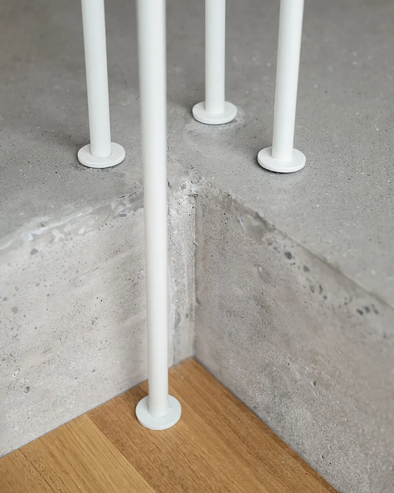 Detail of white steel railing posts meeting polished concrete floor and timber tread at stair corner