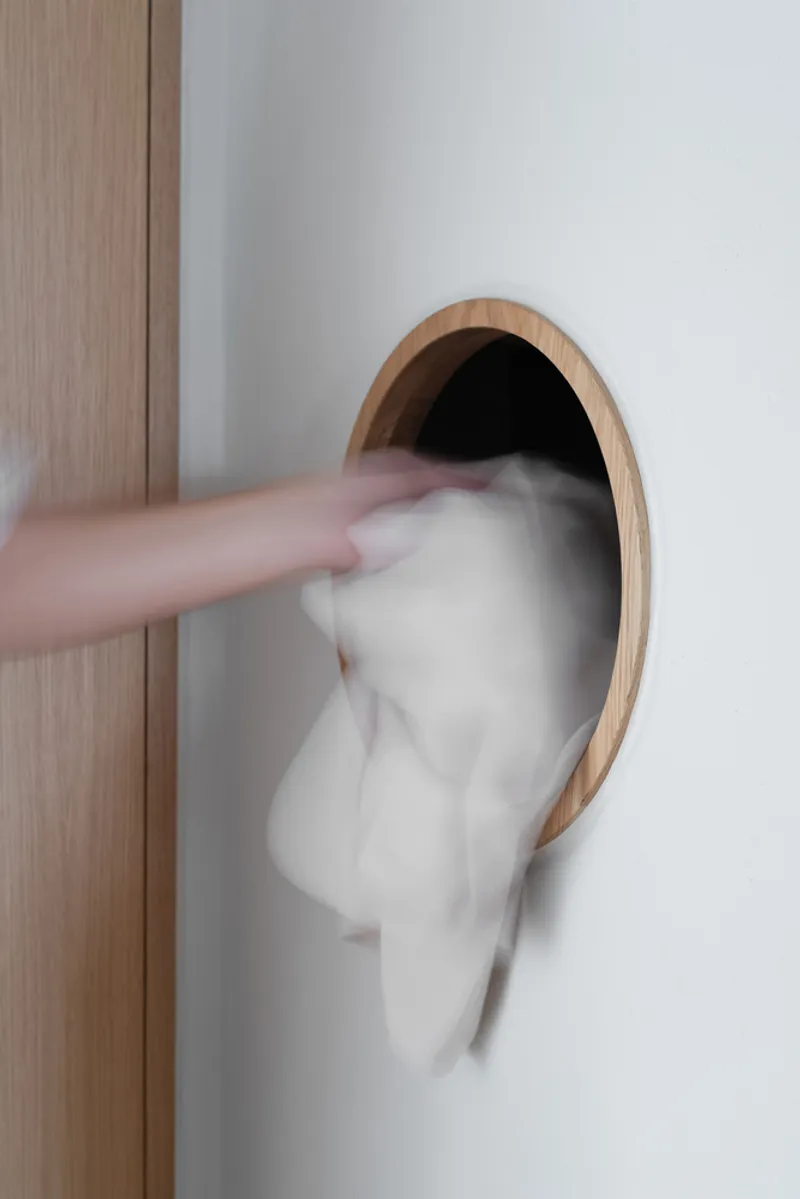 Motion-blurred figure reaching through an oval timber-framed opening in a white wall beside wood paneling